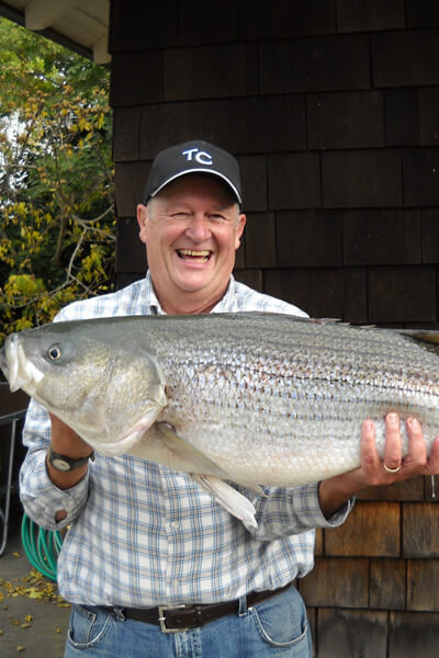 Innkeeper is wearing a blue plaid shirt and holding a 40 pound striped bass