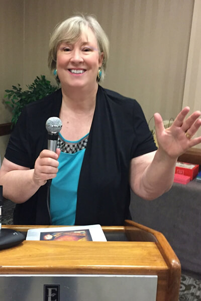 Innkeeper is holding a silver and black microphone behind a light wood podium