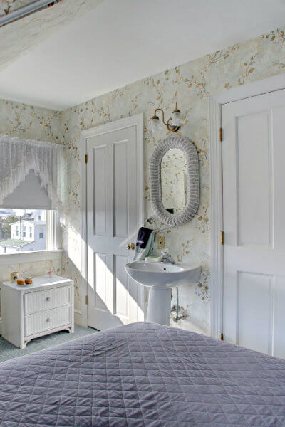 white pedestal sink, white wicker vanity and chair and tall dresser with TV