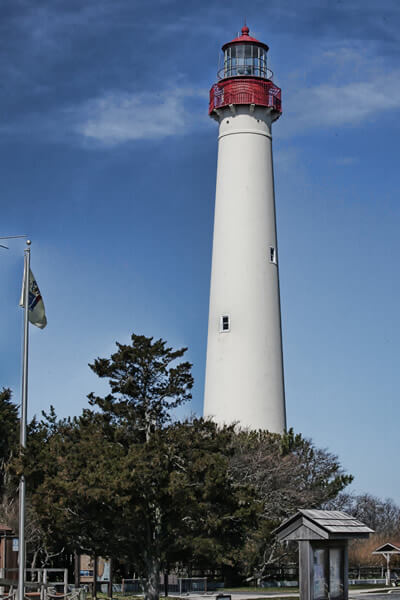white lighthouse with red top with yellow flag of New Jersey and large tree