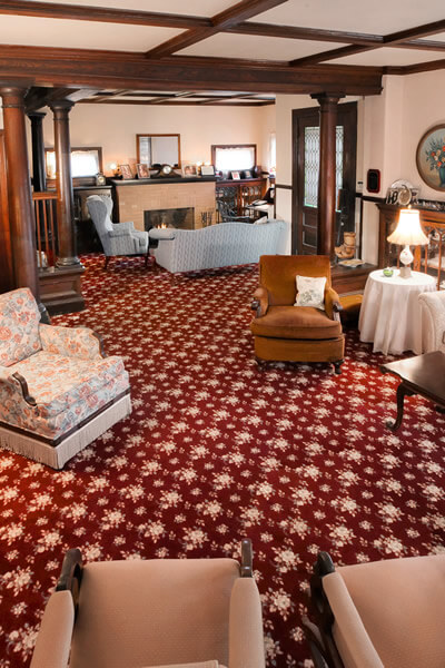 living room with maroon and white carpet, American chestnut beams and pillars and ecru lace curtains