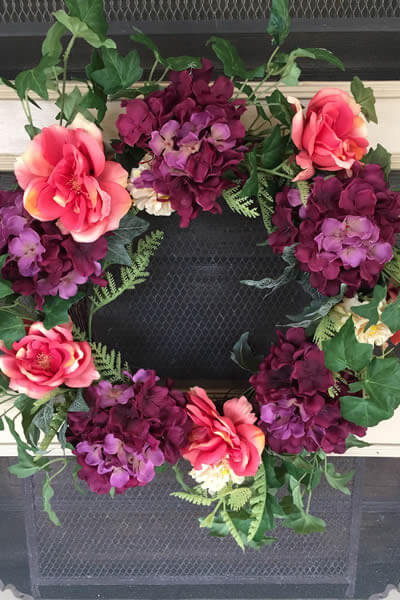 wreath with pink roses and purple hydrangeas hanging on front beige door