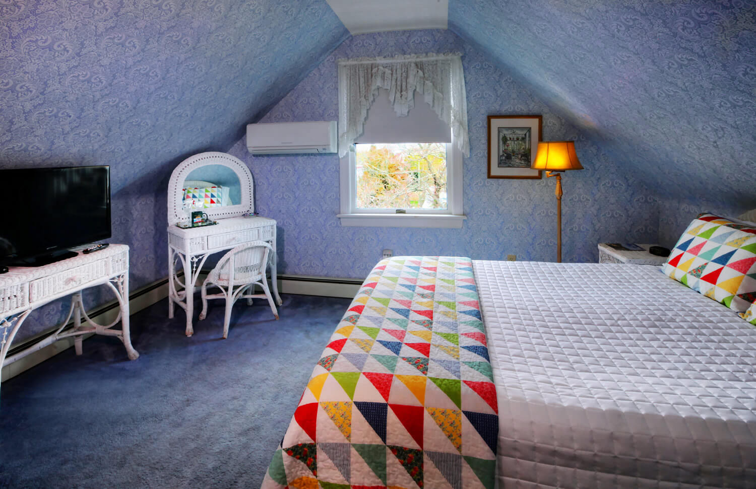 white quilt with brightly colored blanket at bottom of bed, floor lamp, and white wicker