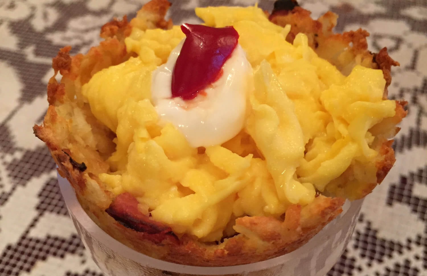 breakfast cupcake filled with scrambled eggs and topped with a dollop of white sour cream and red pimento