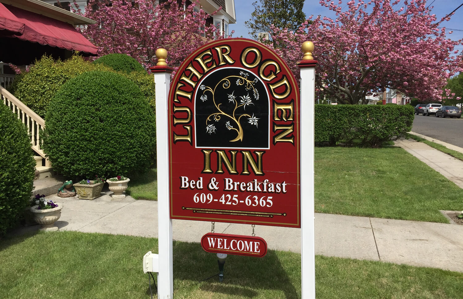 maroon sign with gold letters and 2 white posts with pink flowering tree in background